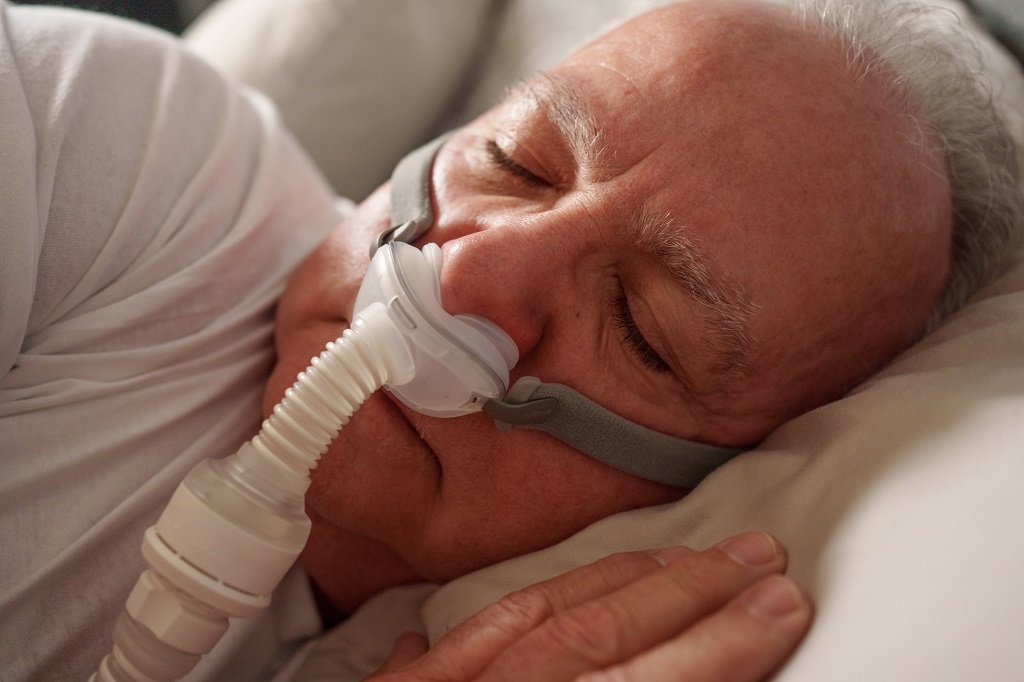 Mature man asleep wearing his CPAP mask to treat his sleep apnea.